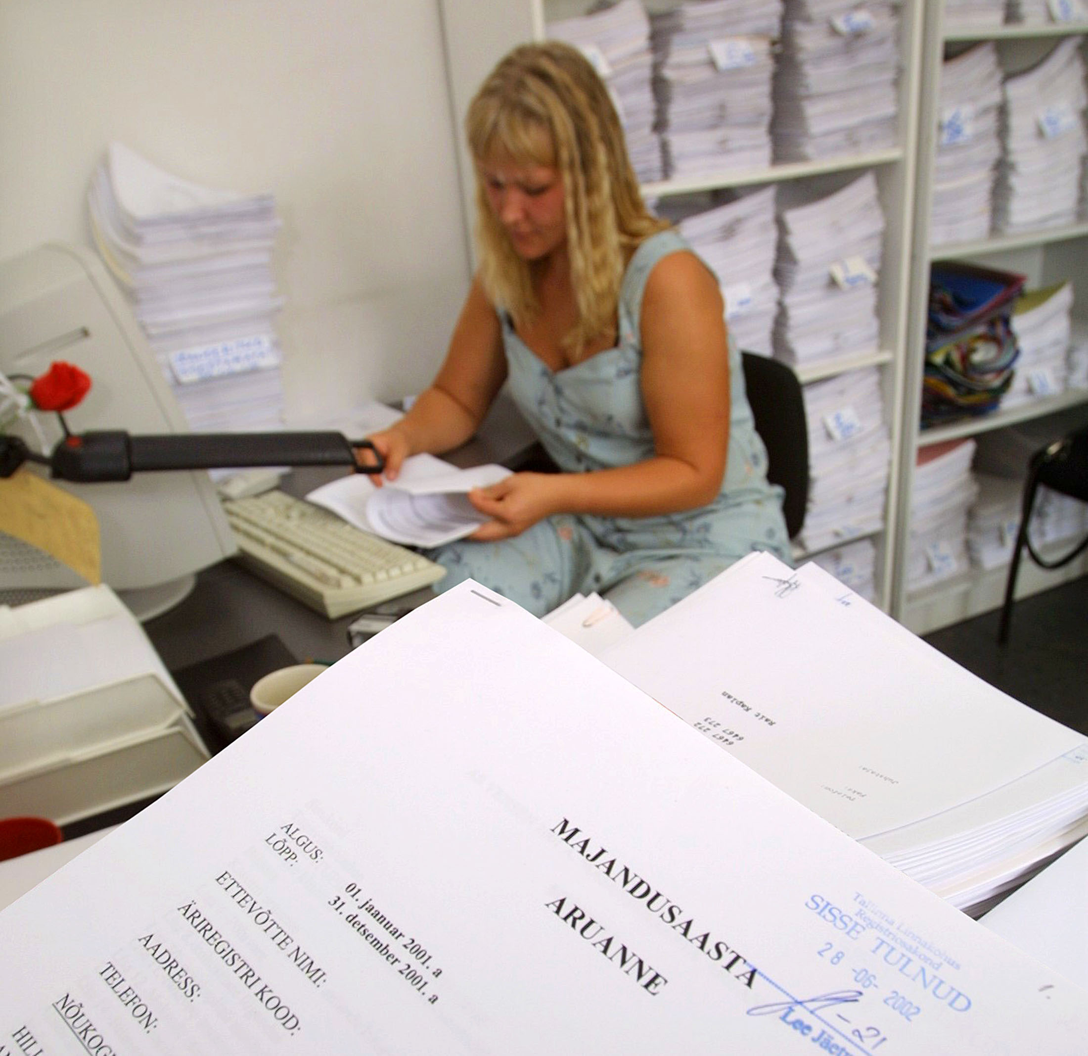 tehniline sekretär sisestamas astaaruandeid arvutisse.taamal kapp täis aruandeid, mis ootavad töötlemist